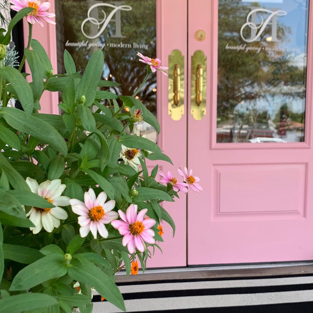 Pink French doors with gold plated handles and glass windows etched with the Talulah & HESS logo with pretty greenery and pink flowers in the foreground. 
