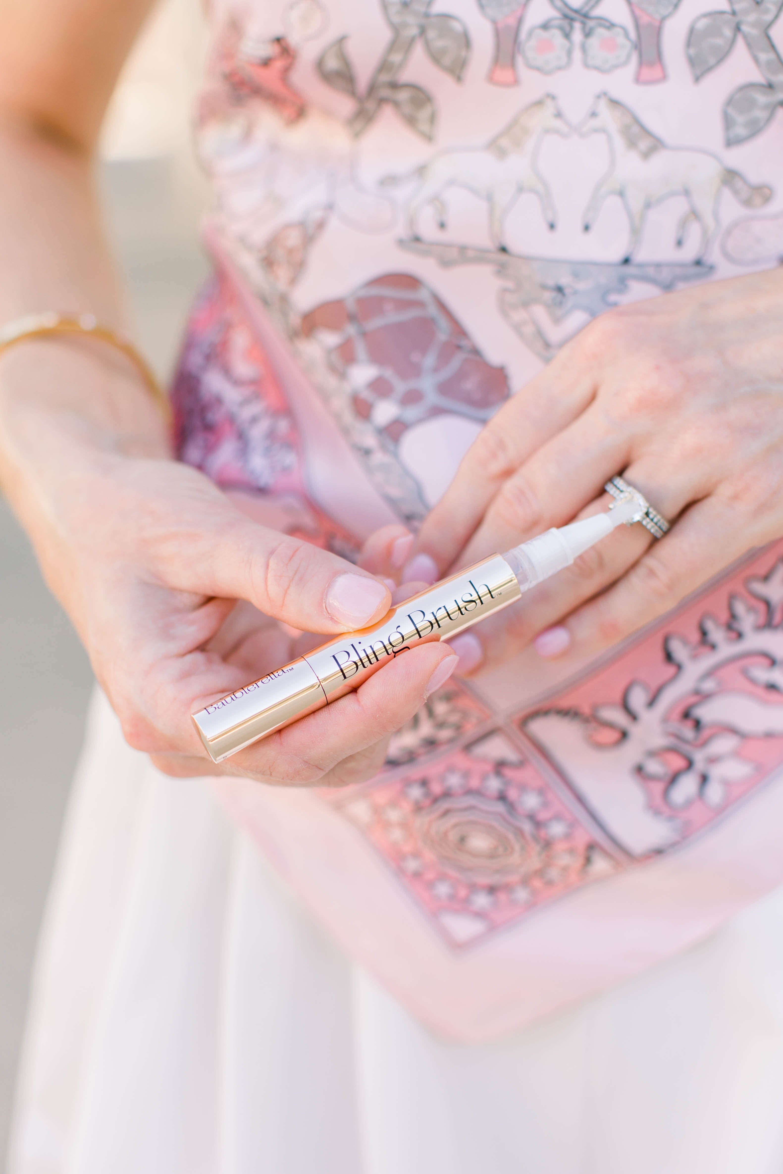 Girl wearing a pink satin scarf top with safari animals and white shorts. She is cleaning her diamond ring with the Bling Brush rinse free jewelry cleaning pen. 